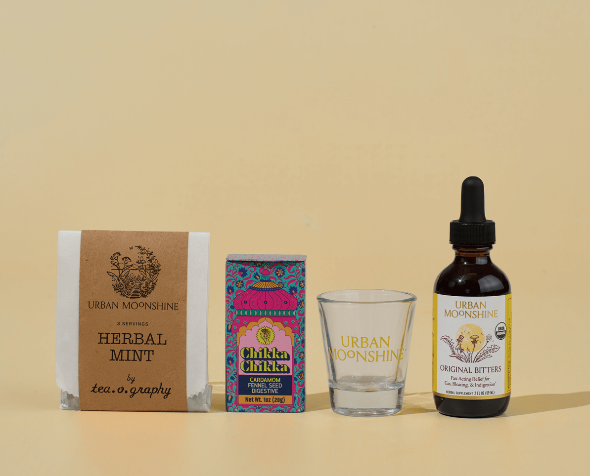 Collection of Urban Moonshine products including a bottle, box, and glass on a beige background