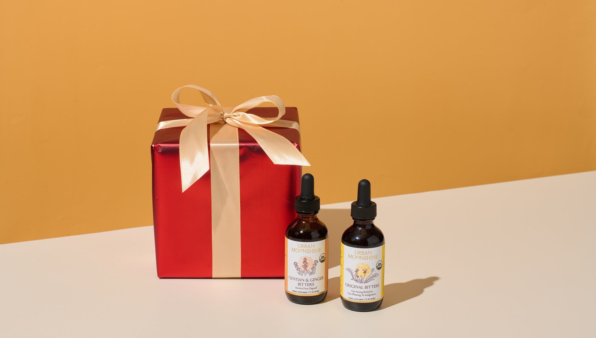 Two dropper bottles and a red gift box in front of an orange background