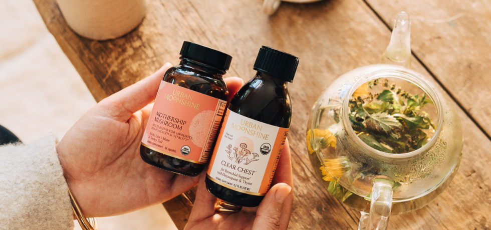 Two bottles of urban moonshine products in hands with a teapot in the background