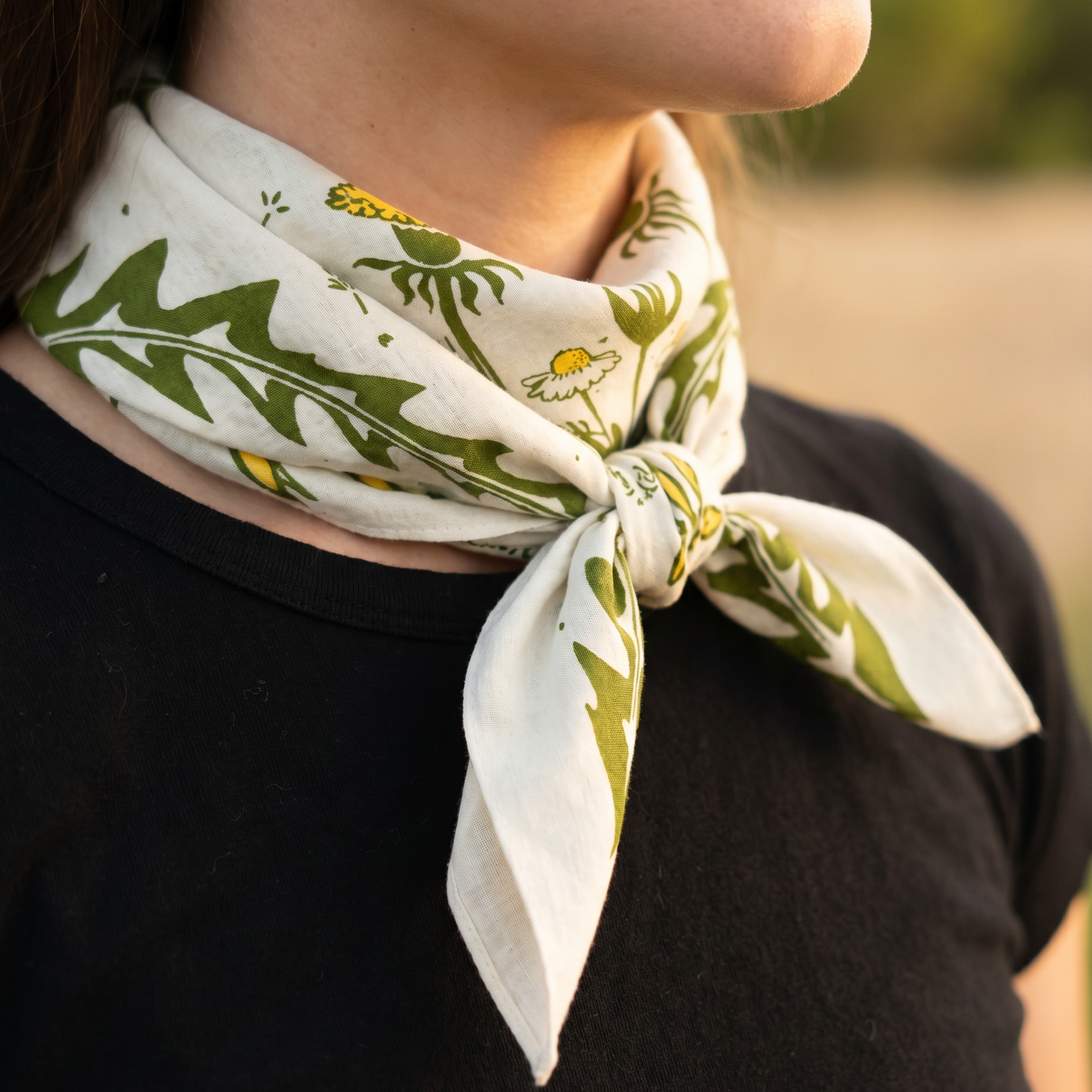 Person wearing a white bandana with green leaf pattern on a blurred natural background