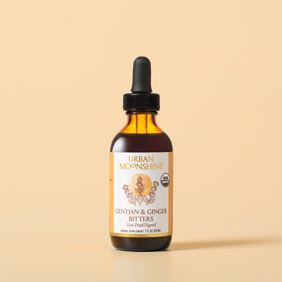 Urban Moonshine Gentian & Ginger Bitters in an amber glass bottle with a black dropper cap, set against a solid beige background.