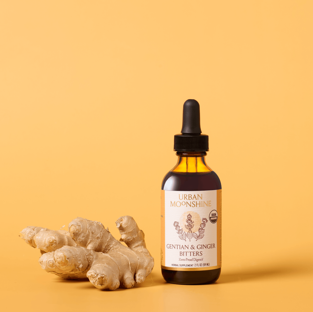 A bottle of Urban Moonshine Gentian & Ginger Bitters next to fresh ginger roots on a warm yellow background.