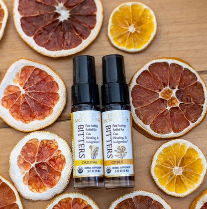 Two bottles of Urban Moonshine Bitters on a wooden surface with dried citrus slices.